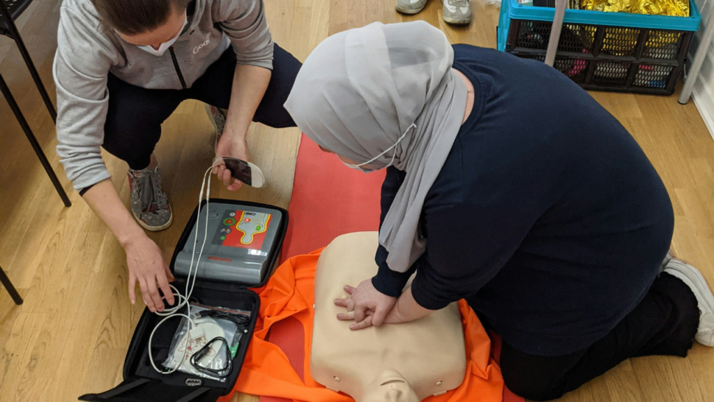 Healthcare trainees practicing CPR on a manikin with defibrillator equipment during emergency response training.